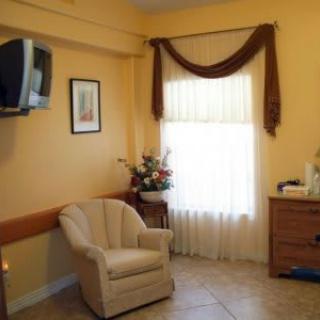 A cozy living room interior featuring a comfortable chair, a window with curtains, and a mounted television.