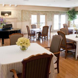 A well-decorated dining area with tables and chairs, featuring a piano and floral arrangements.