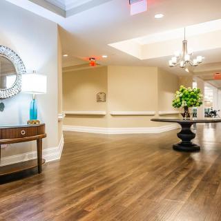 A spacious and elegantly decorated lobby with wood flooring, featuring a side table with a decorative mirror and a central round table adorned with flowers.