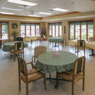 A spacious dining hall with round tables and chairs, illuminated by natural light from large windows.