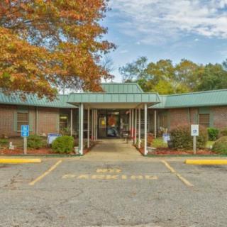 A brick building with a green roof surrounded by autumn trees and a parking lot.