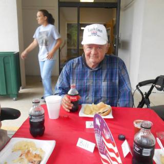 A man sitting at a table with food and drinks, wearing a plaid shirt and a hat.