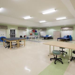An open and well-lit rehabilitation therapy room equipped with various treatment tables and exercise equipment.