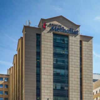 A modern office building with a prominent logo on the facade against a clear blue sky.