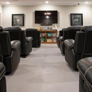A cozy home theater room with comfortable leather seating arranged in rows, facing a large screen.
