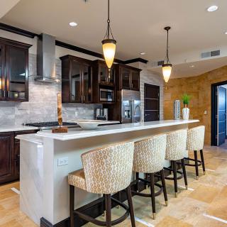 A modern kitchen featuring a marble countertop island with bar stools and pendant lighting.