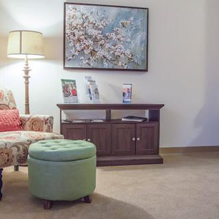 A cozy living room corner featuring a floral artwork, comfortable chair, and decorative lamp.