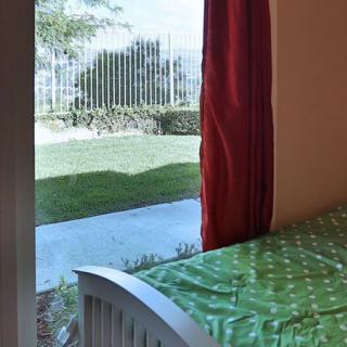 A bedroom with a green bedspread, red curtains, and a view of the garden through the window.