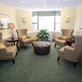 A cozy seating area with upholstered chairs and a central ottoman, decorated with warm lighting and a potted plant.