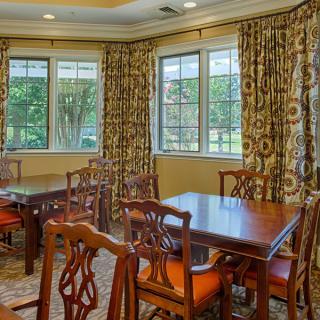 Elegant dining room with wooden tables and chairs, complemented by patterned curtains and large windows.