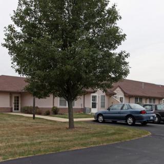 A suburban building with a tree in the foreground and cars parked in the driveway.