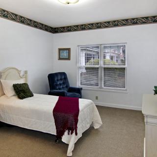 A cozy bedroom with a single bed, an upholstered chair, and a window letting in natural light.