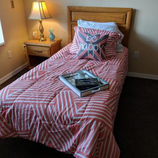 A cozy bedroom with a single bed featuring a striped bedspread and decorative pillow, accompanied by a nightstand and lamp.