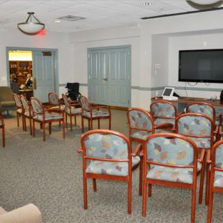 An empty waiting room with rows of chairs facing a television screen.