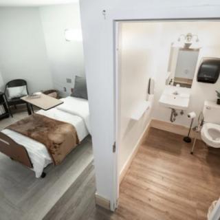 A hospital room with an adjoining bathroom, featuring a patient bed and medical equipment.