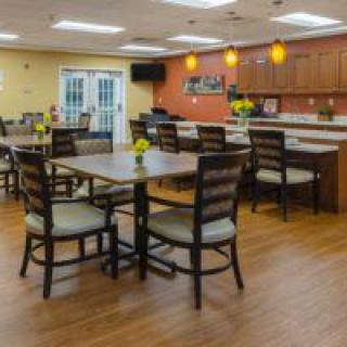 A modern dining area with tables and chairs, featuring wood flooring and warm lighting.