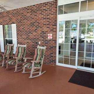 A cozy porch area with three rocking chairs facing a brick wall and glass entrance.