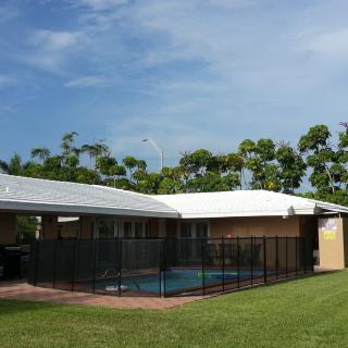 A suburban house with a fenced swimming pool and a green lawn on a sunny day.