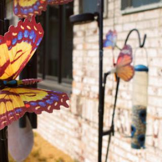 A colorful butterfly decoration near a hummingbird feeder in a tranquil garden setting.