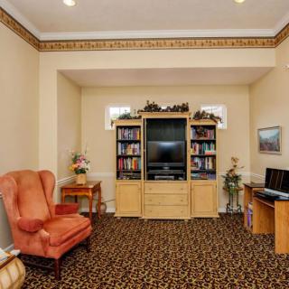 A cozy living room with a television, bookshelves, an armchair, and a home office setup.