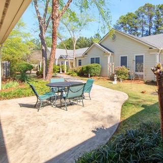 A sunny patio with a table and chairs, surrounded by a garden and trees.