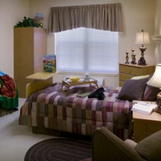 A cozy bedroom interior featuring a bed, lamp, and various furniture items.