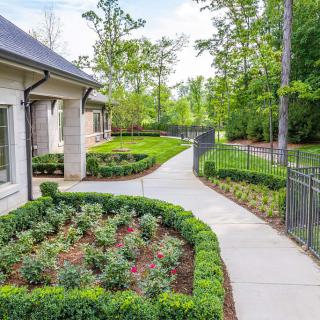 A well-maintained garden with a pathway surrounded by lush greenery and a house in the background.