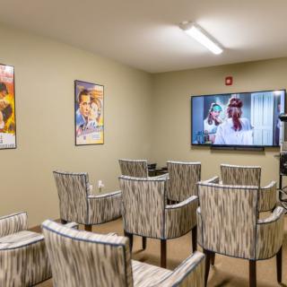 A cozy home theater room with neatly arranged chairs, a large screen displaying a movie, and film posters adorning the walls.
