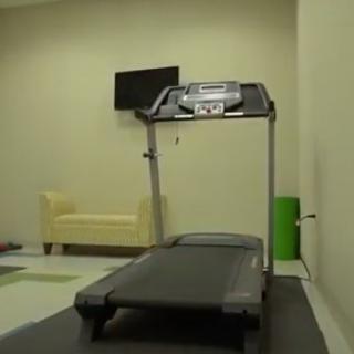 An indoor gym with a treadmill, TV, and sofa.