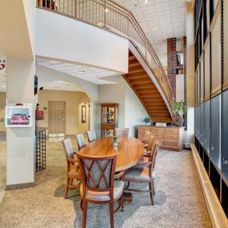 A modern office interior with a conference table and chairs set near large windows and a stylish staircase.