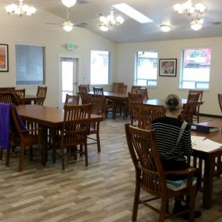 An empty dining area with wooden tables and chairs, featuring multiple windows and elegant lighting fixtures.