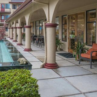 A modern building facade with columns and outdoor seating, featuring landscaped greenery.