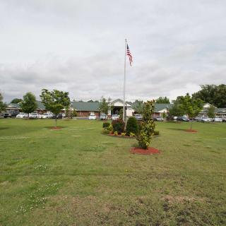 A park with a flagpole surrounded by a grassy area and trees under a cloudy sky.