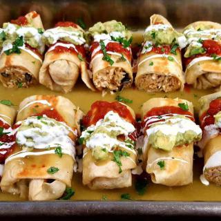 A tray of baked chimichangas topped with guacamole, sour cream, and salsa.