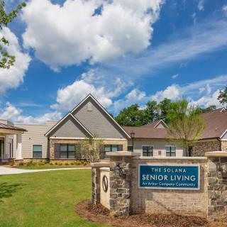 A senior living facility surrounded by a well-maintained lawn and trees under a partly cloudy sky.