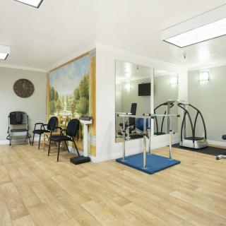 A therapy room equipped with exercise machines and chairs, featuring mirrors and a wooden floor.