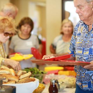 A group of people serving themselves food at a buffet table during a social gathering.