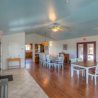 A spacious dining area with wooden flooring, multiple tables and chairs, illuminated by natural light.