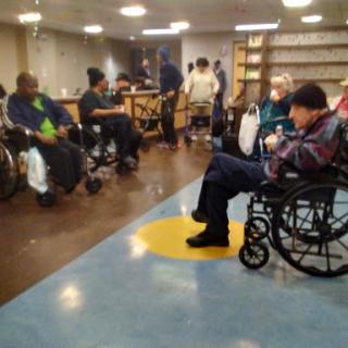 A community space in a care facility with several elderly individuals in wheelchairs engaging with each other.