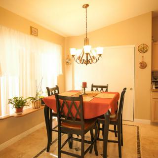 A cozy dining room with a table set for four, illuminated by a chandelier and natural light from a large window.