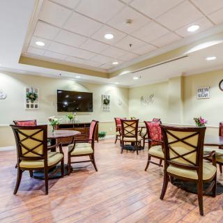 A well-lit dining area featuring several tables and chairs, with a television mounted on the wall.