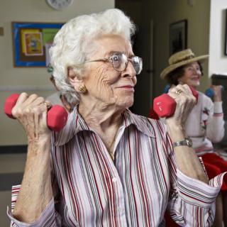 An elderly woman lifting pink dumbbells and staying active.