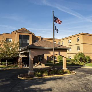 A hotel entrance with a driveway, featuring flags waving on poles.