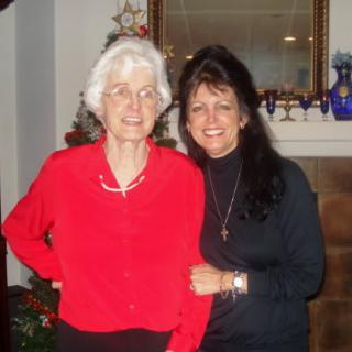 Two women smiling in front of a Christmas tree indoors.