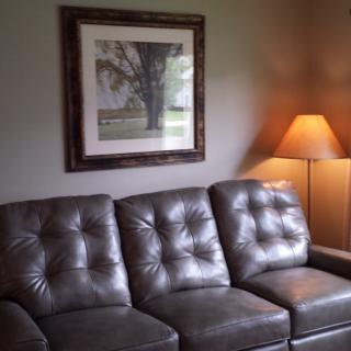 A cozy living room with a leather sofa, a floor lamp, and framed wall art.