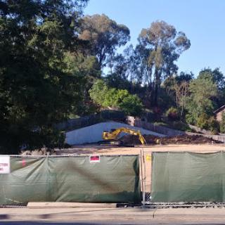 Ongoing demolition work in a residential area, with construction equipment visible behind a green fence.