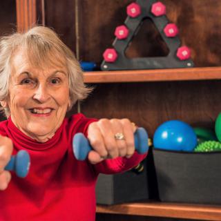 A senior woman smiling while lifting dumbbells as part of her exercise routine.
