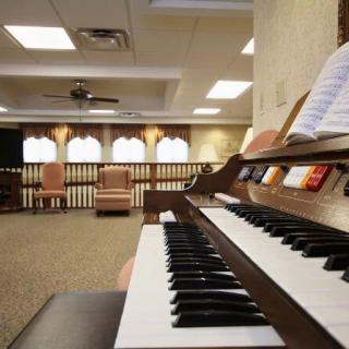 A piano in a spacious room with chairs and music sheets.