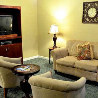 A cozy living room with a sofa, two armchairs, a TV stand, and a coffee table, warmly lit by a standing lamp.