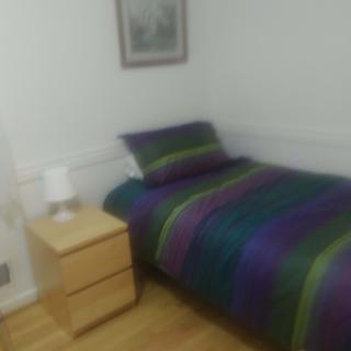 A cozy bedroom with a single bed adorned with striped bedding, next to a wooden nightstand and lamp.